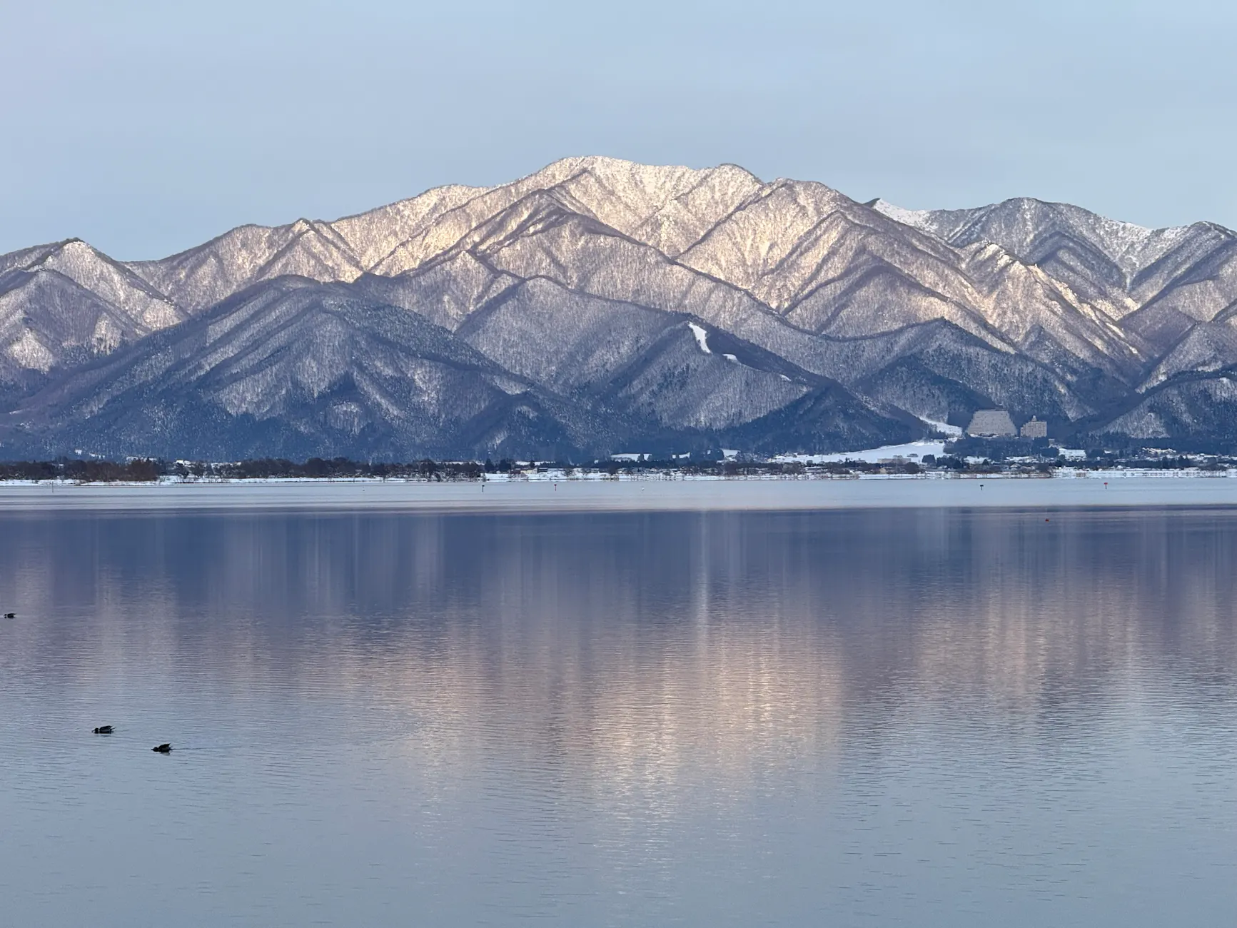 Snow-covered mountains reflecting in a calm lake during winter.