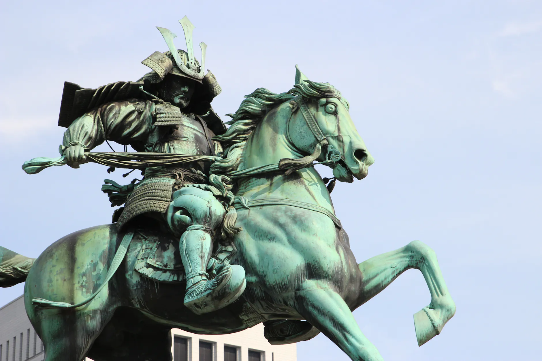A striking bronze statue of a samurai on horseback, displayed against a vibrant sky.