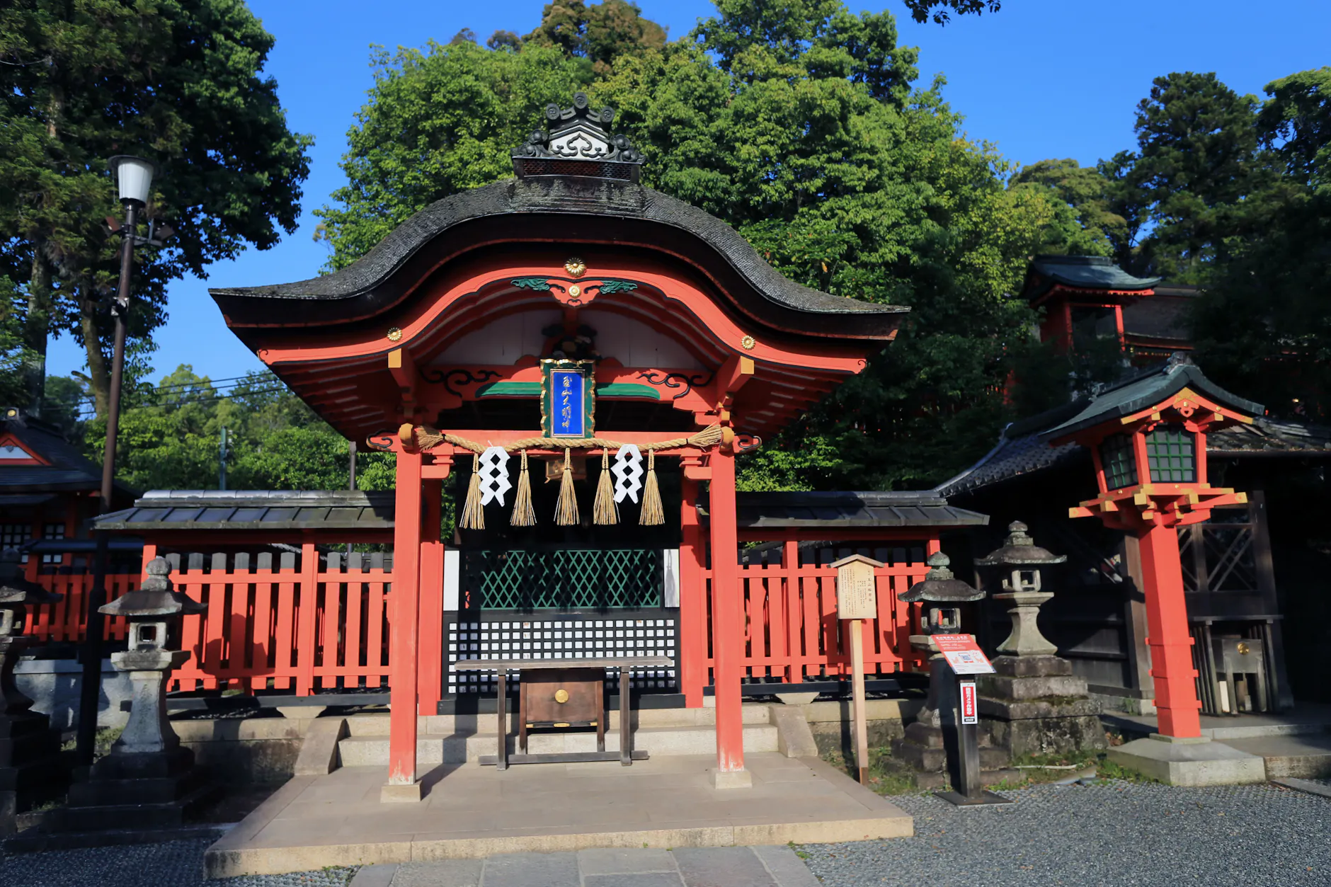 A stunning view of a traditional Japanese shrine with vibrant red accents surrounded by lush greenery under a blue sky.
