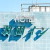 Brightly lit hotel sign with blue tiles under a clear sky, showcasing modern architecture.