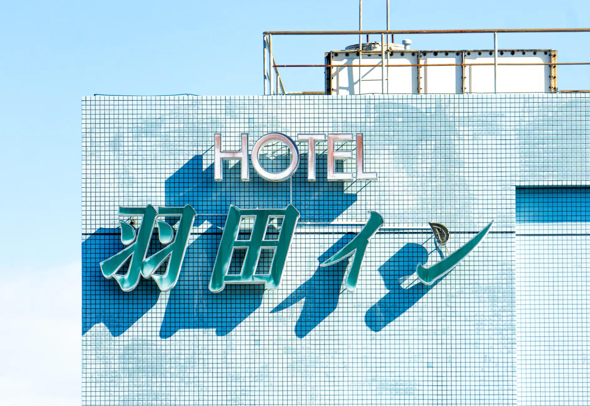 Brightly lit hotel sign with blue tiles under a clear sky, showcasing modern architecture.