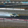 Car performing a drift maneuver on a race track with smoke trailing behind.