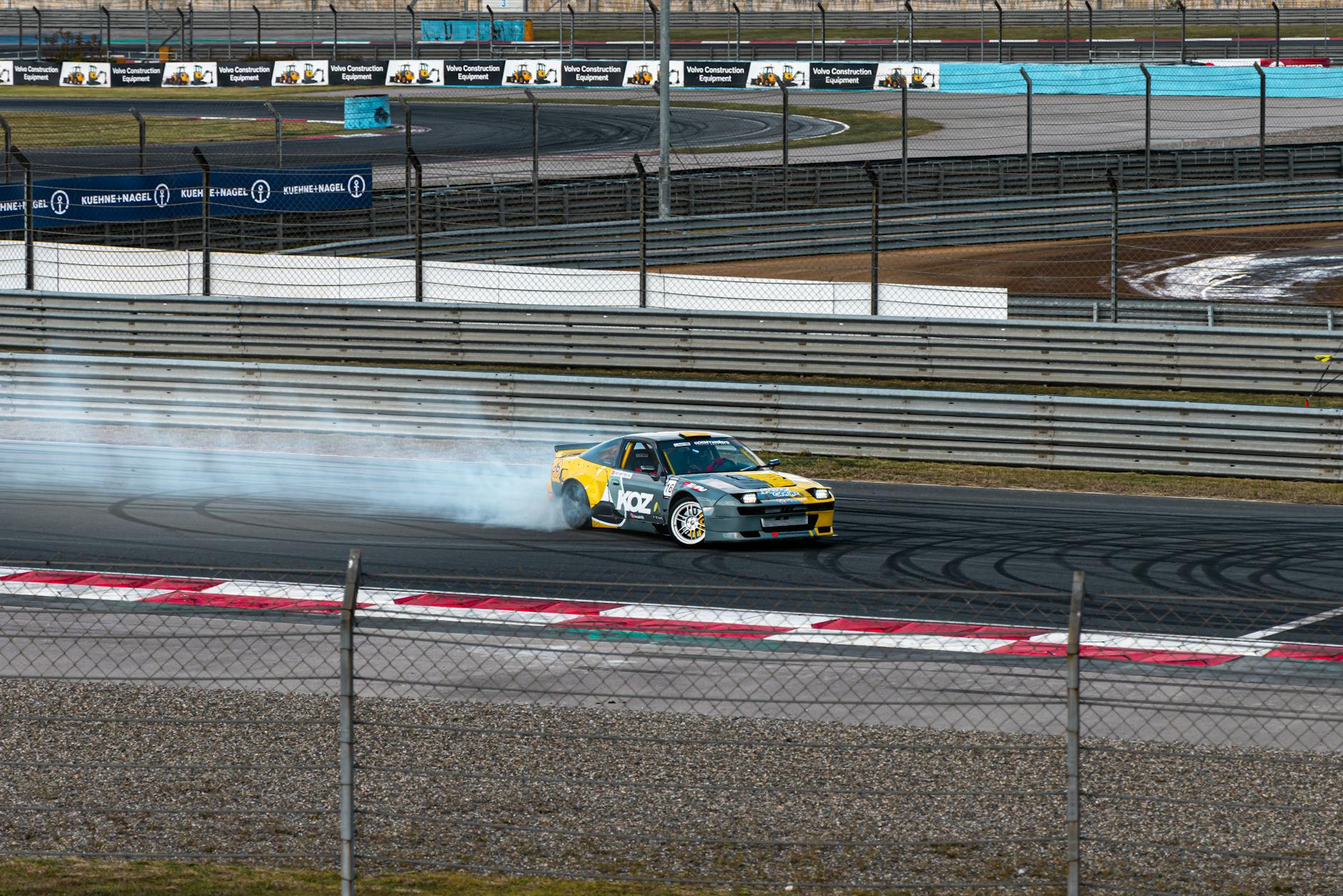 Car performing a drift maneuver on a race track with smoke trailing behind.