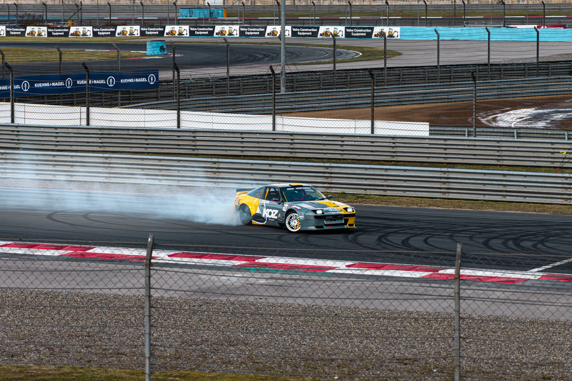Car performing a drift maneuver on a race track with smoke trailing behind.