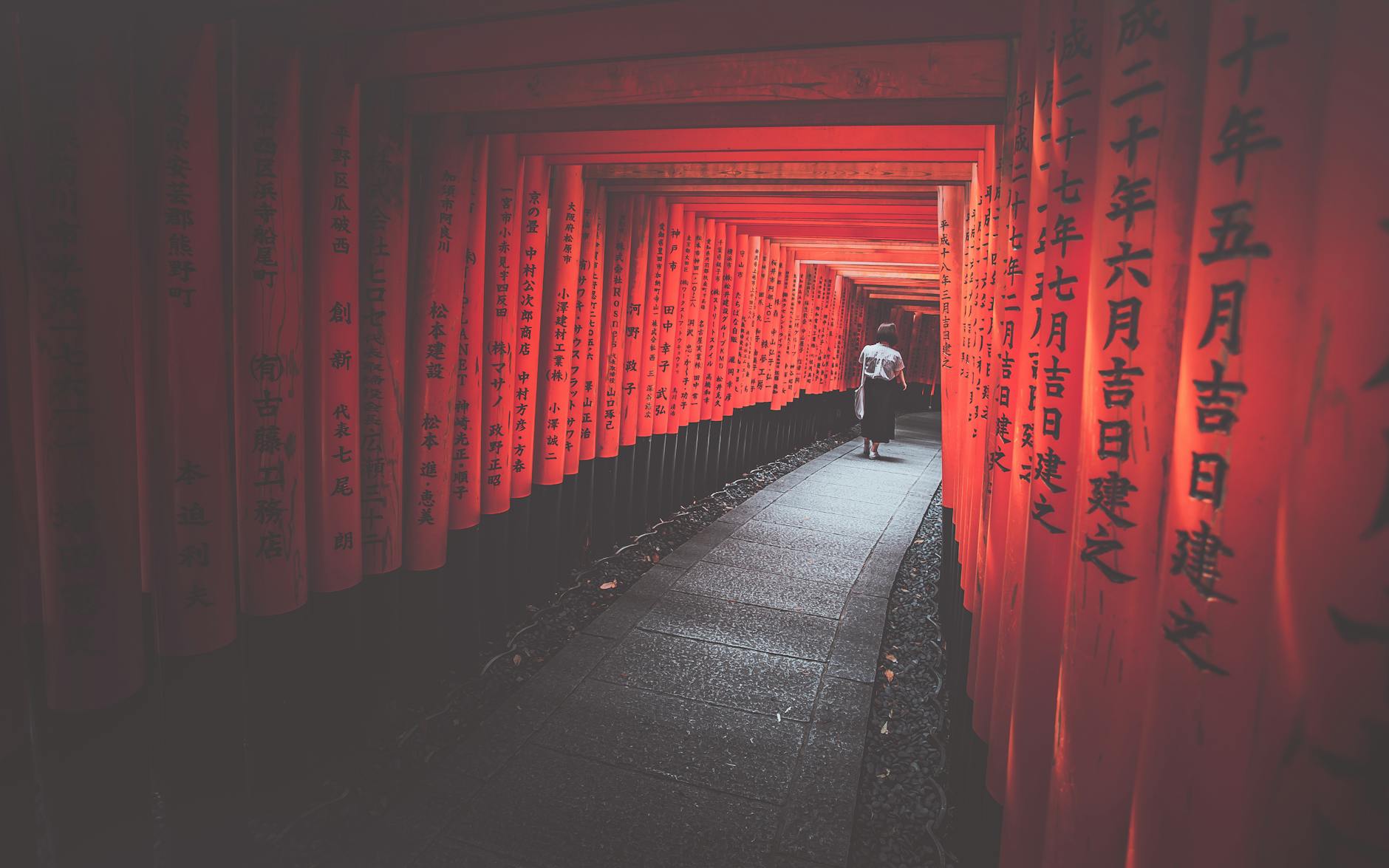 A woman walks through the iconic red torii gates of Fushimi Inari Taisha in Kyoto, Japan.