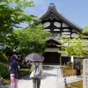 Visitors at a traditional temple in Kyoto, Japan surrounded by lush greenery and historic architecture.