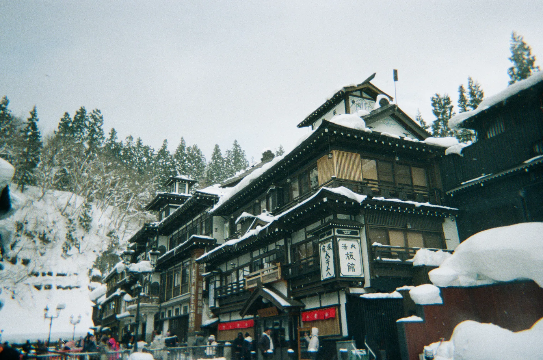 A picturesque view of traditional Japanese architecture in a snowy onsen town, set against a backdrop of snow-covered trees.