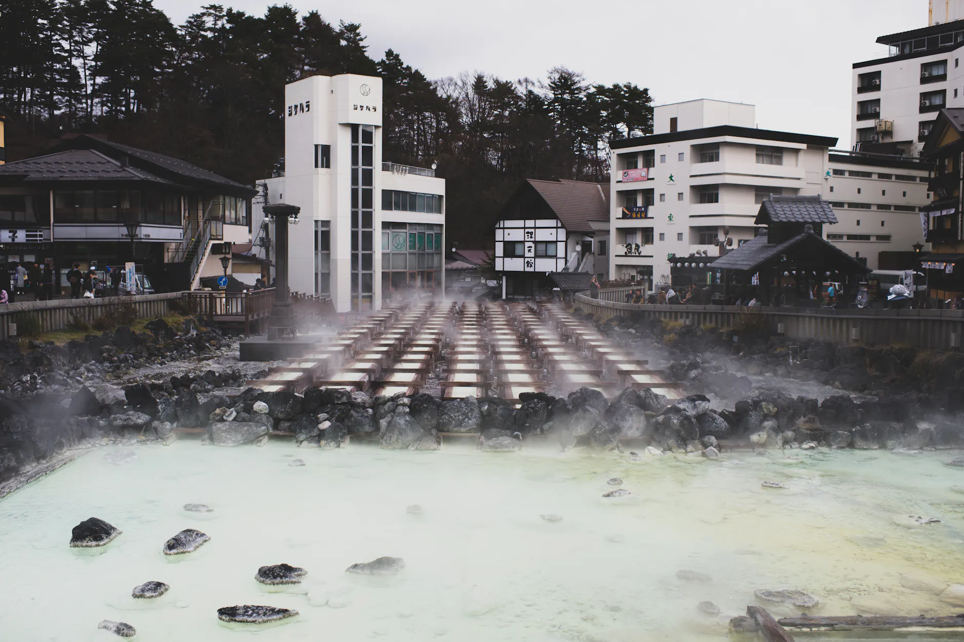 A tranquil hot spring town with steam rising from mineral-rich waters, surrounded by traditional architecture.