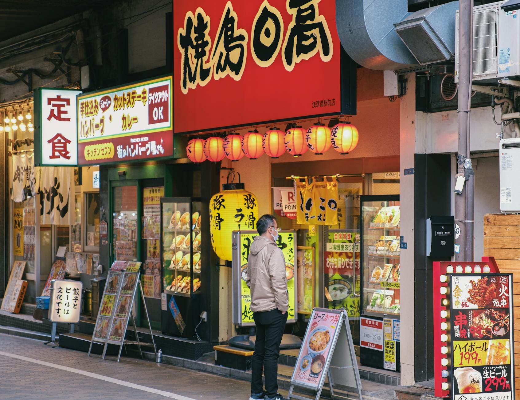 A man stands outside a Japanese restaurant in a lively street, examining the menu. Bright signage and Japanese characters create an inviting atmosphere.