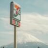 A sign for a convenience store with Mount Fuji in the background under a clear sky.