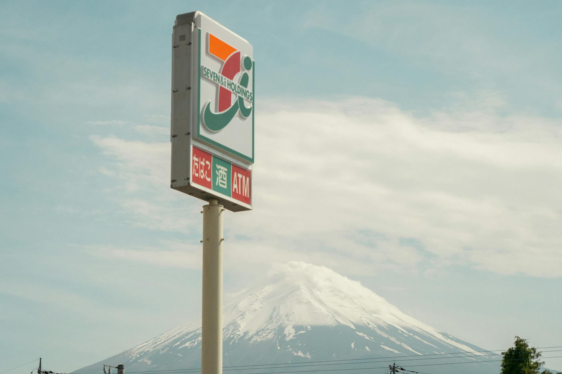 A sign for a convenience store with Mount Fuji in the background under a clear sky.