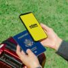 Hands holding a smartphone with eSIM and a passport near a luggage outdoors, ideal for travel concepts.