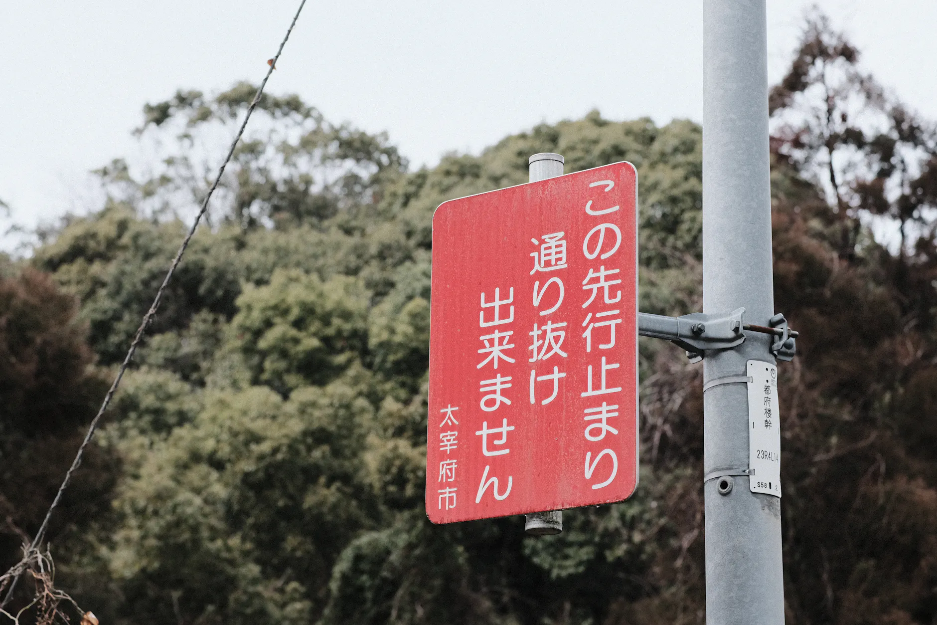 A red traffic sign against a forested backdrop in Fukuoka, Japan, depicting a no-through road message.