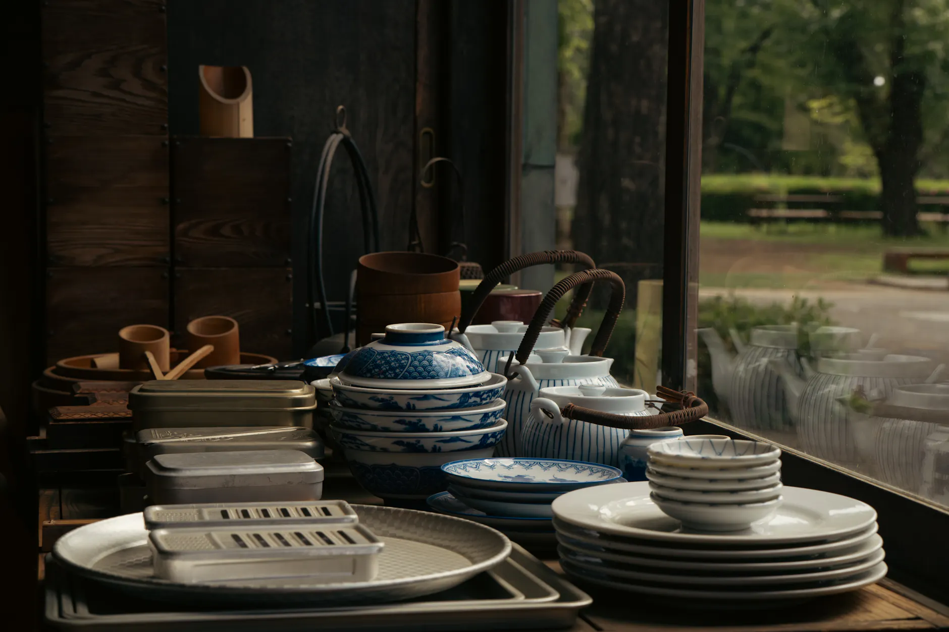 A serene view of Japanese ceramic dishware elegantly arranged by a window offering an outdoor glimpse.