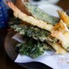 Japanese tempura set featuring shrimp and vegetables on a dark plate
