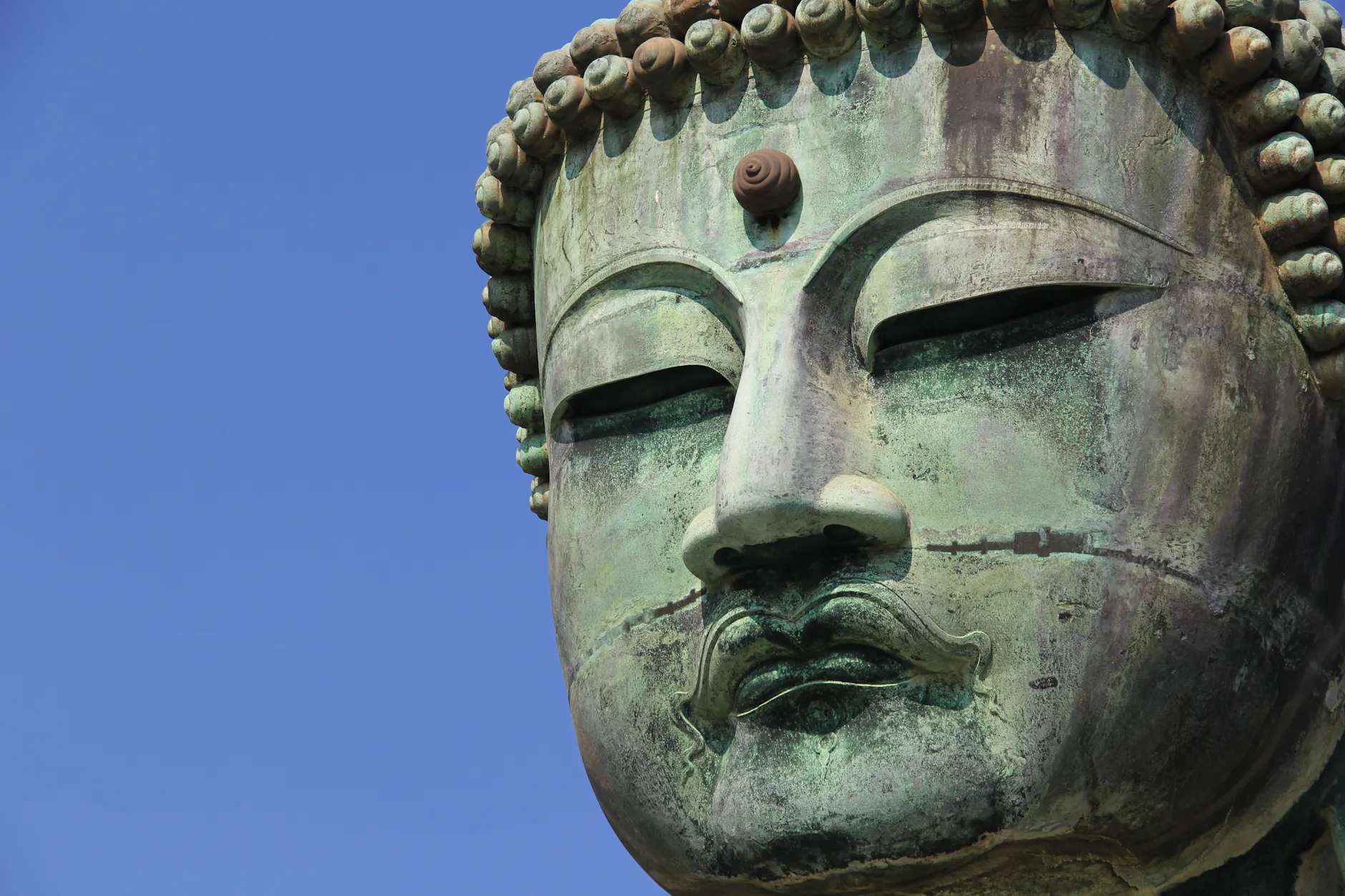 Detailed close-up of the Kamakura Daibutsu Buddha statue under a clear blue sky in Japan.