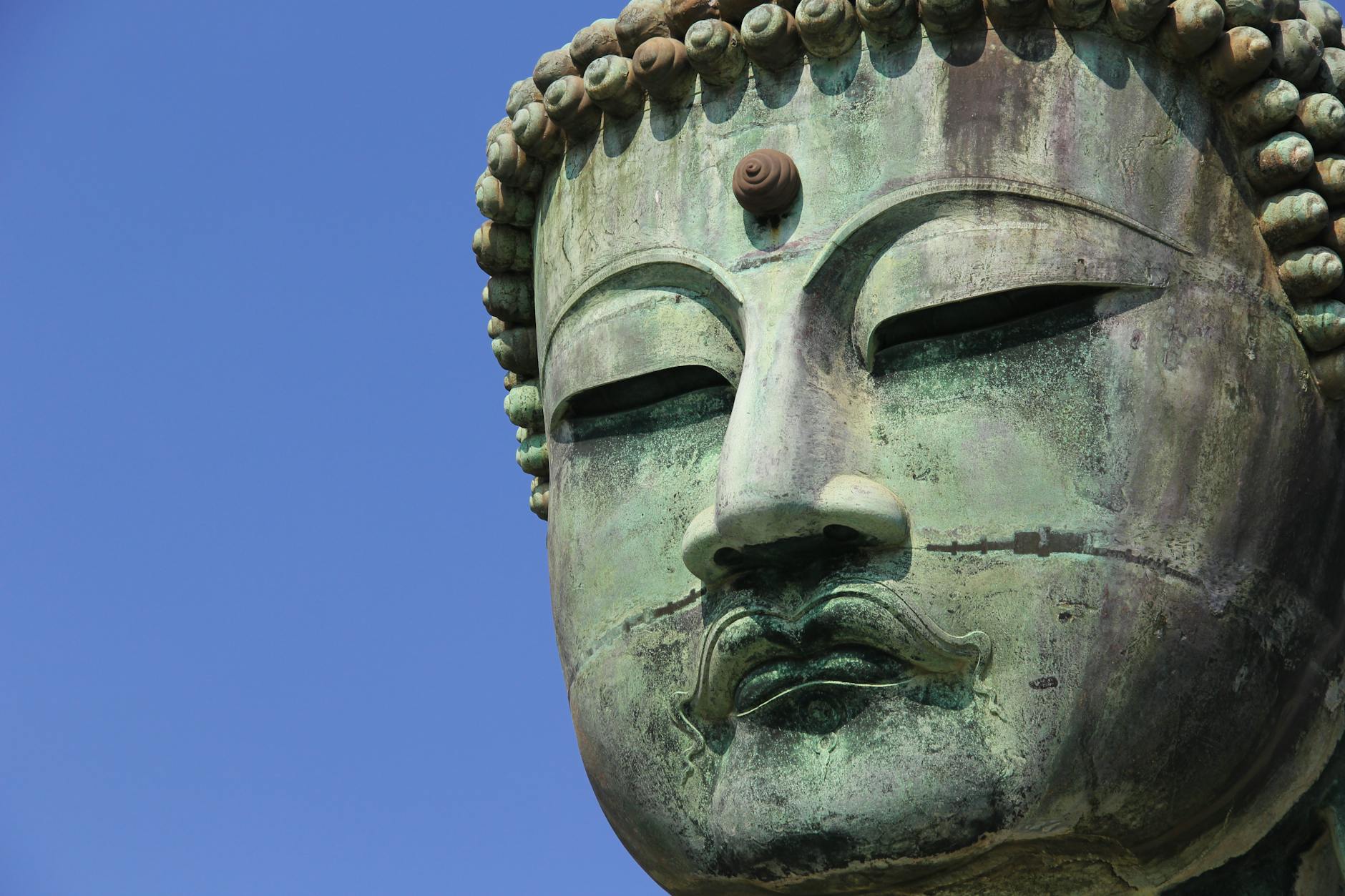 Detailed close-up of the Kamakura Daibutsu Buddha statue under a clear blue sky in Japan.