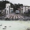 A tranquil hot spring town with steam rising from mineral-rich waters, surrounded by traditional architecture.