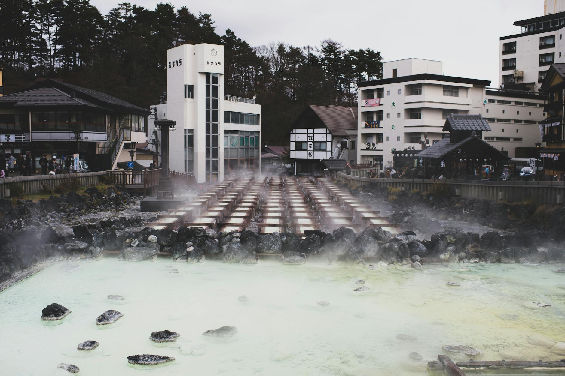 A tranquil hot spring town with steam rising from mineral-rich waters, surrounded by traditional architecture.