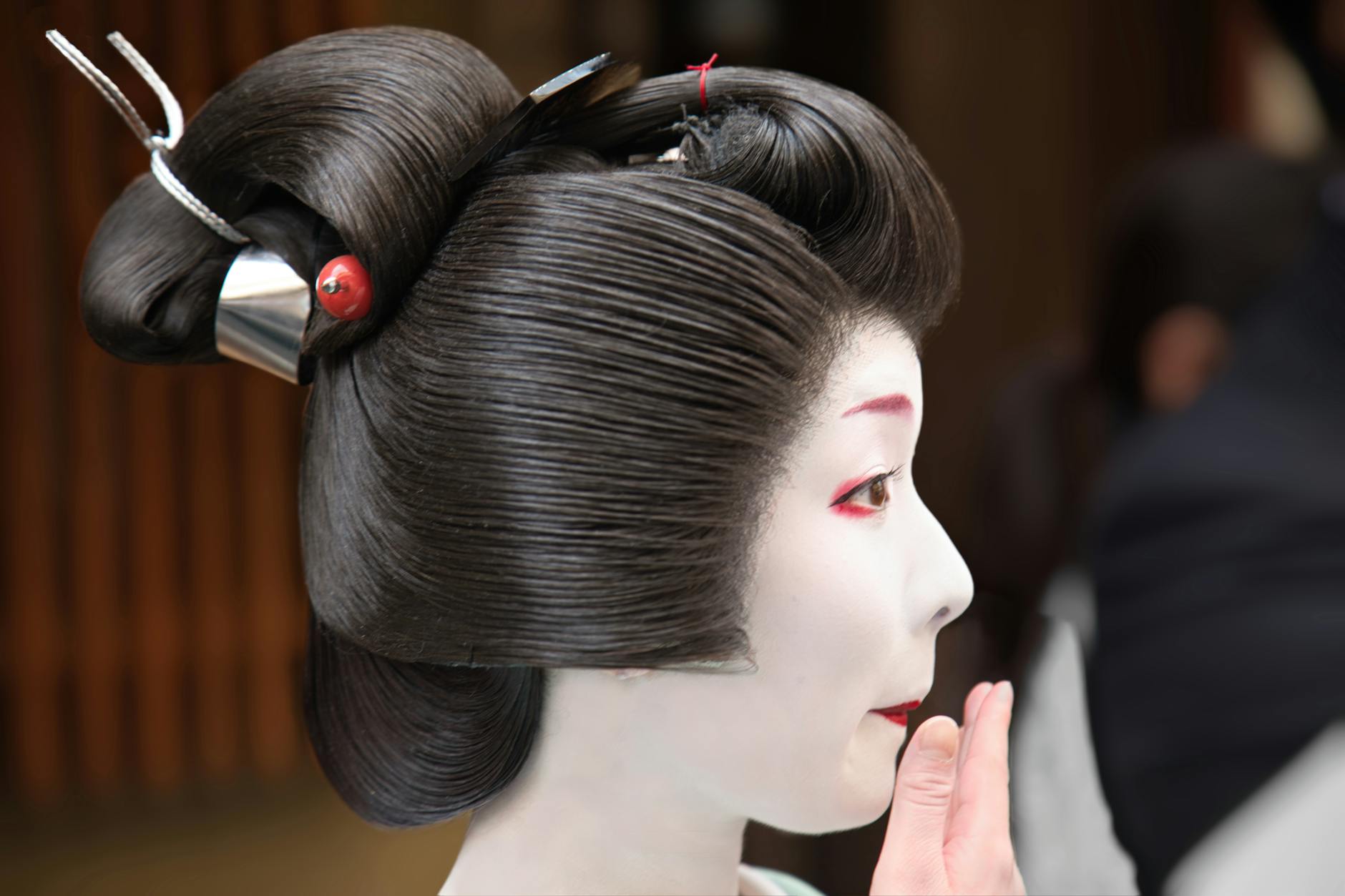 Close-up of a maiko in Kyoto wearing traditional kimono and applying makeup, symbolizing Japanese culture.