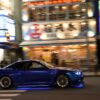 Dynamic shot of a blue sports car speeding through vibrant Tokyo streets at night.