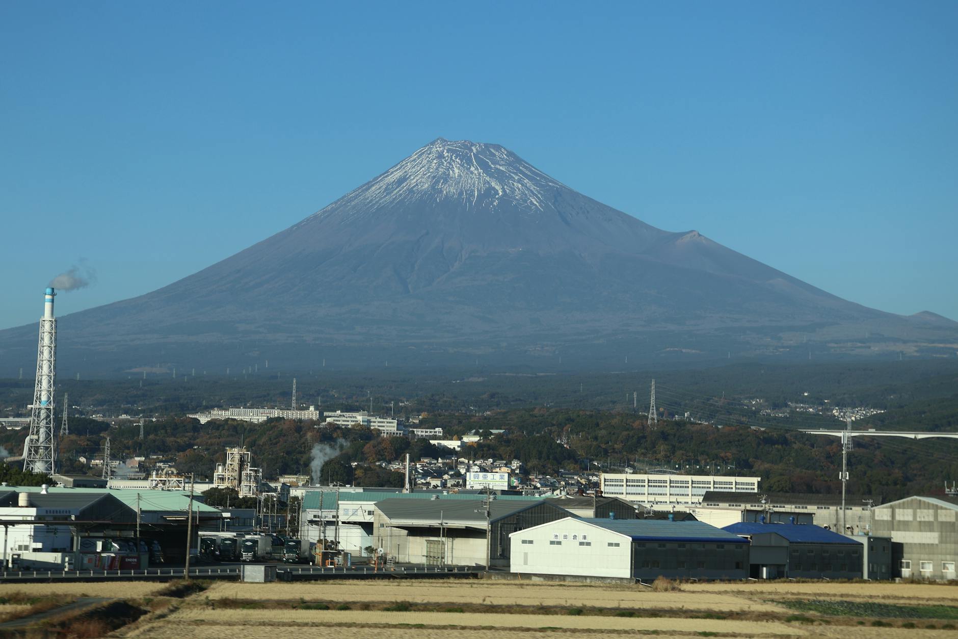 Mount Fuji towers over the industrial backdrop in Oyama, Shizuoka, Japan. Clear skies highlight this iconic peak.