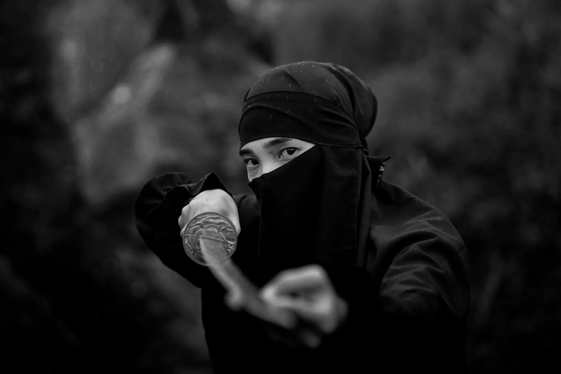 A dramatic black and white photo of a masked samurai warrior wielding a katana, conveying mystery and tradition.