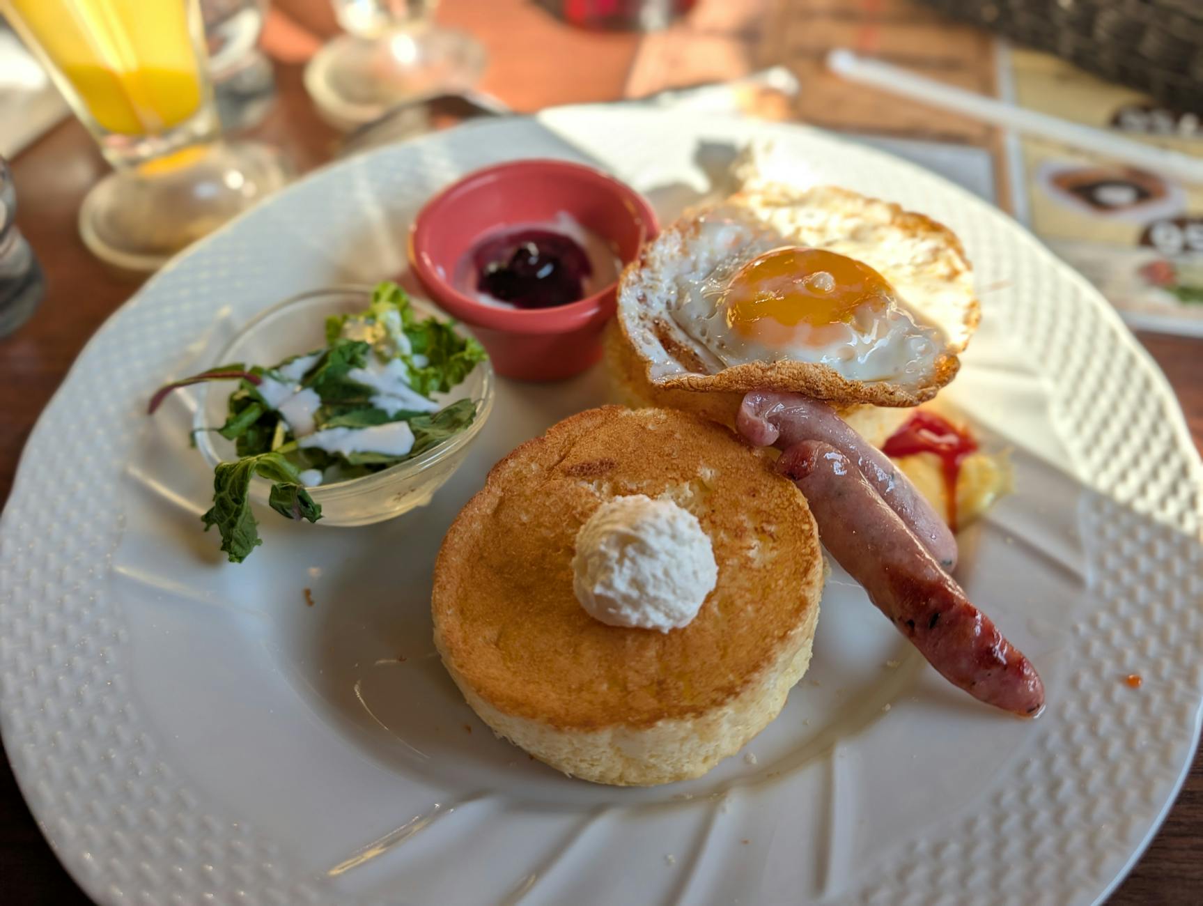 A scrumptious breakfast featuring pancakes, fried egg, sausage, and salad, perfect for a morning meal.