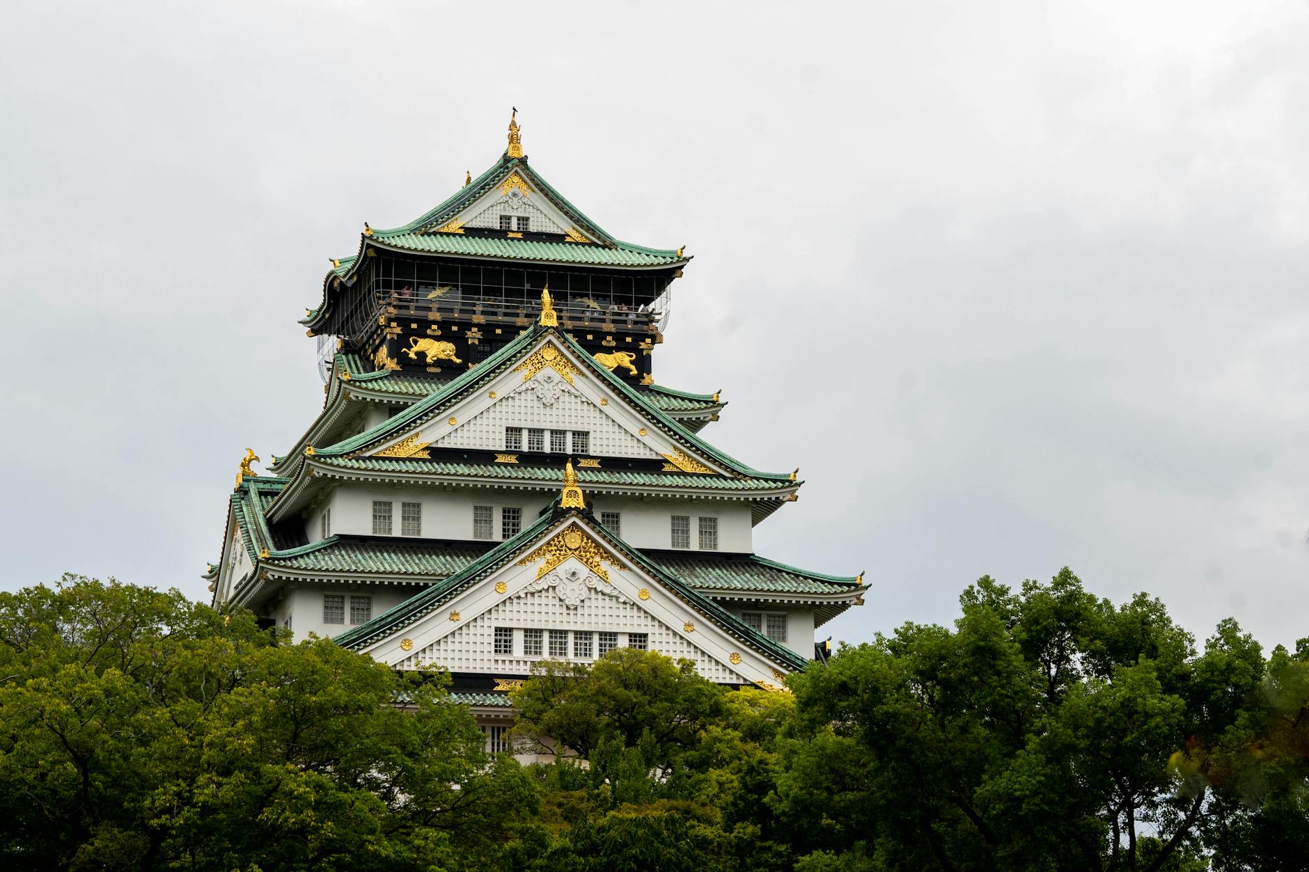 Stunning view of Osaka Castle surrounded by lush greenery under a cloudy sky, epitomizing traditional Japanese architecture.