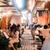 Experience the vibrant nightlife of Osaka's alleyway dining with people enjoying meals and socializing.