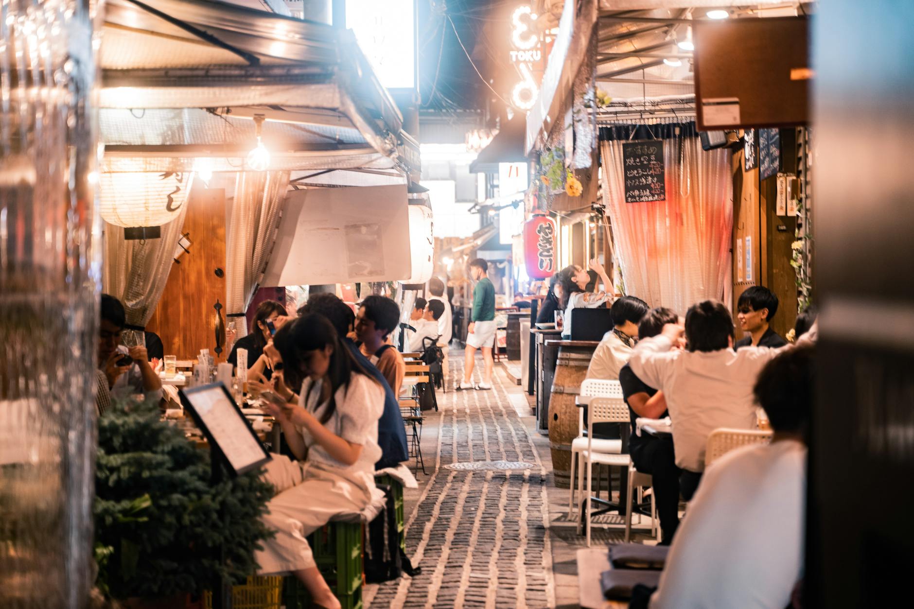 Experience the vibrant nightlife of Osaka's alleyway dining with people enjoying meals and socializing.