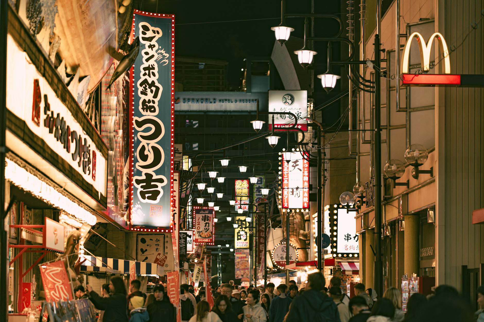 Vibrant night scene capturing the bustling atmosphere of a Japanese street crowded with people and illuminated by neon signs.