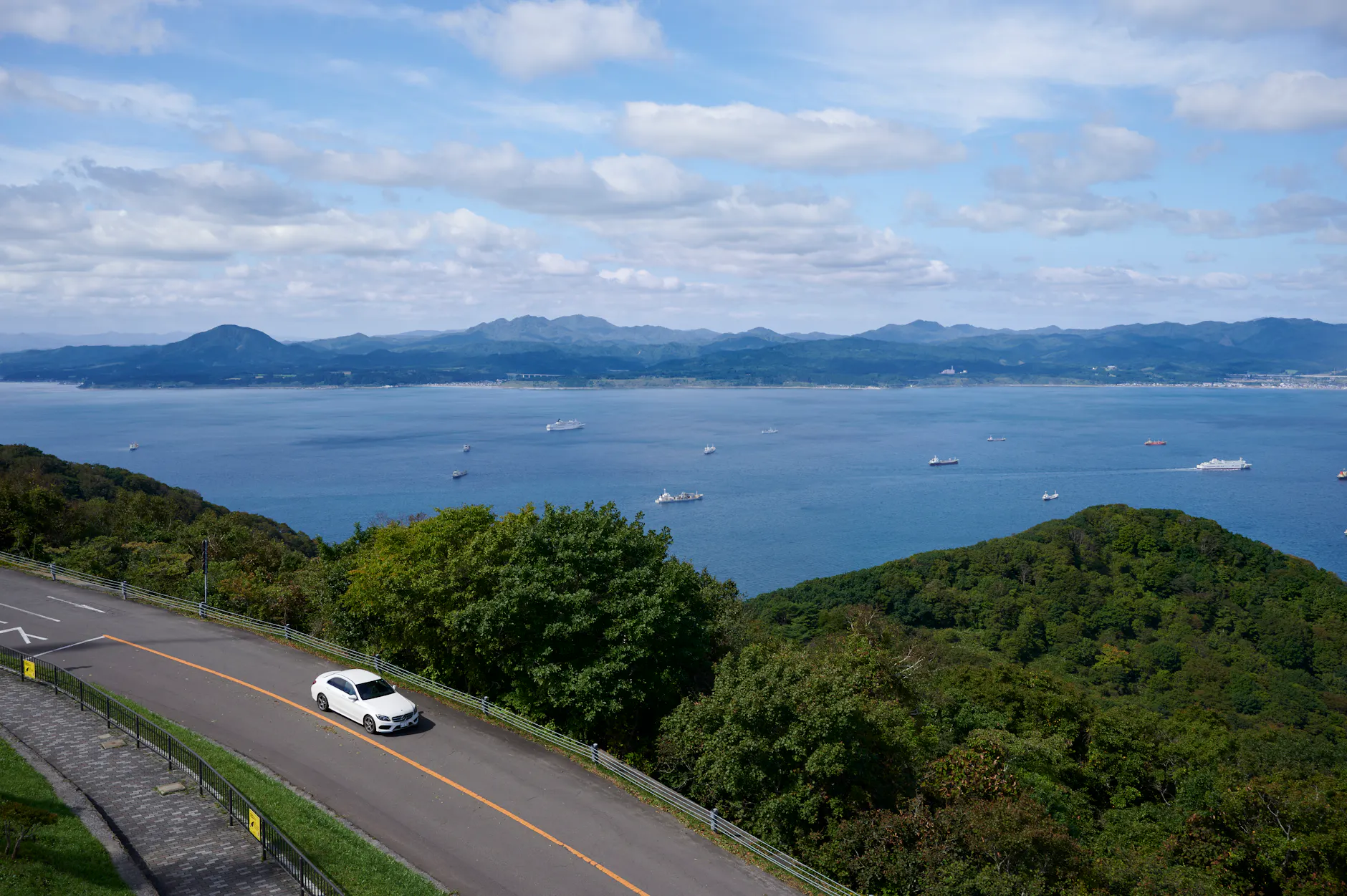Aerial view of a car on a road overlooking Hakodate's coastline and sea in Hokkaido, Japan.