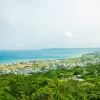 Calm turquoise water of ocean washing shore with small town and green tropical forest under cloudy sky
