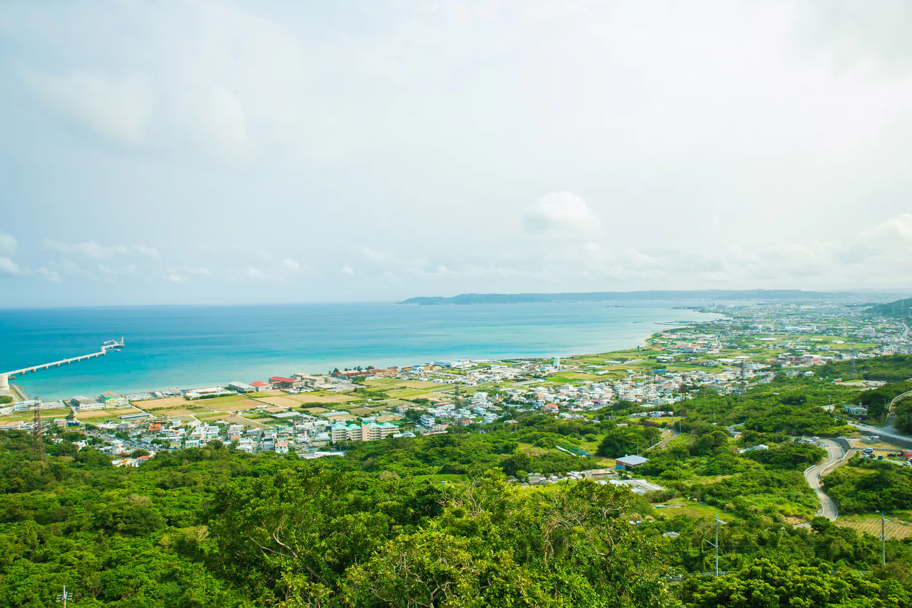 Calm turquoise water of ocean washing shore with small town and green tropical forest under cloudy sky