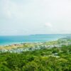 Calm turquoise water of ocean washing shore with small town and green tropical forest under cloudy sky