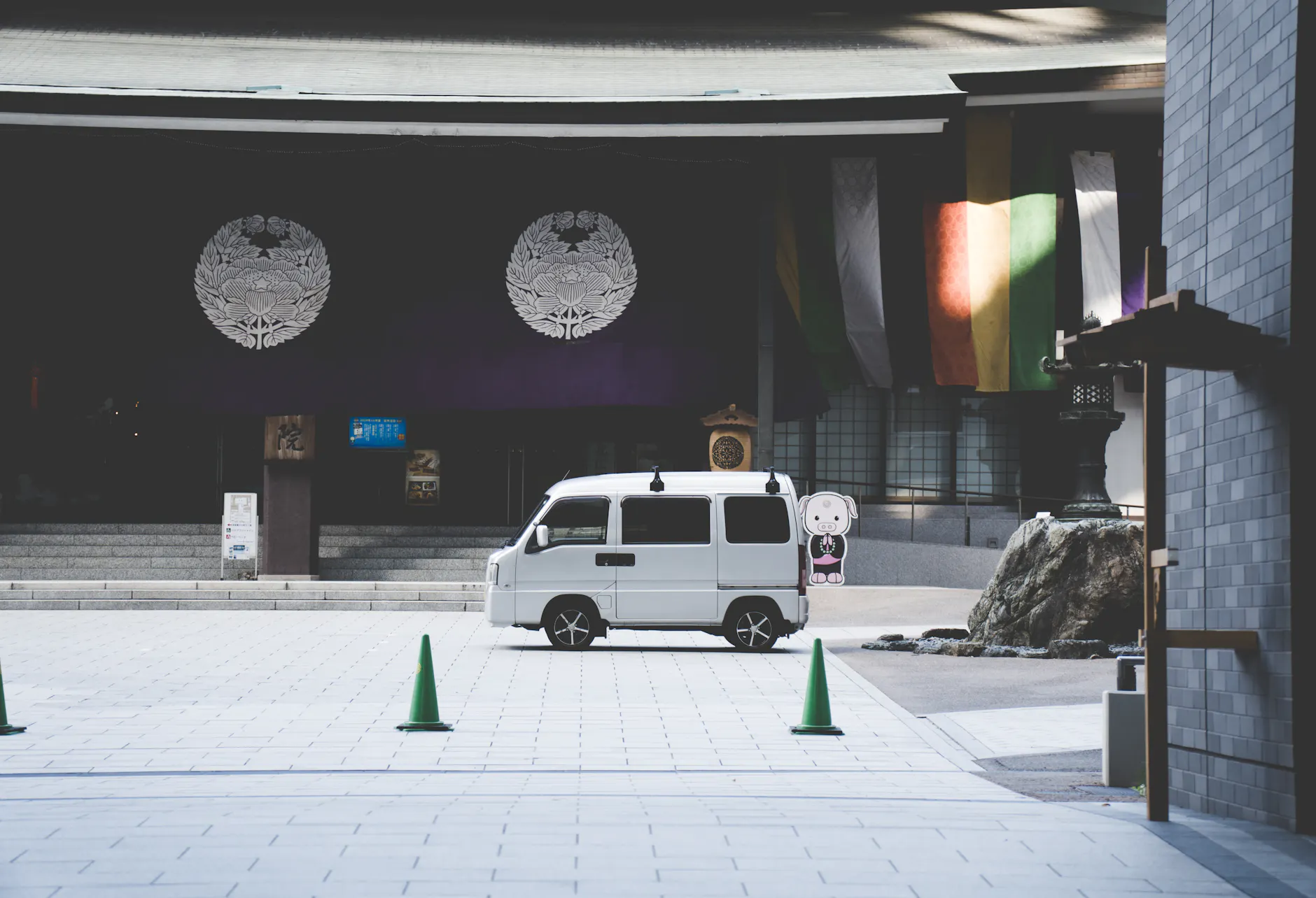White kei van parked in front of an Osaka shrine with colorful banners.