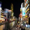 Nighttime view of Dotonbori Canal in Osaka, Japan, with bustling crowds and neon lights.
