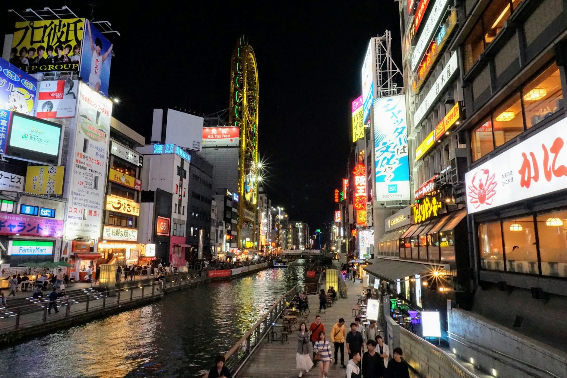 Nighttime view of Dotonbori Canal in Osaka, Japan, with bustling crowds and neon lights.