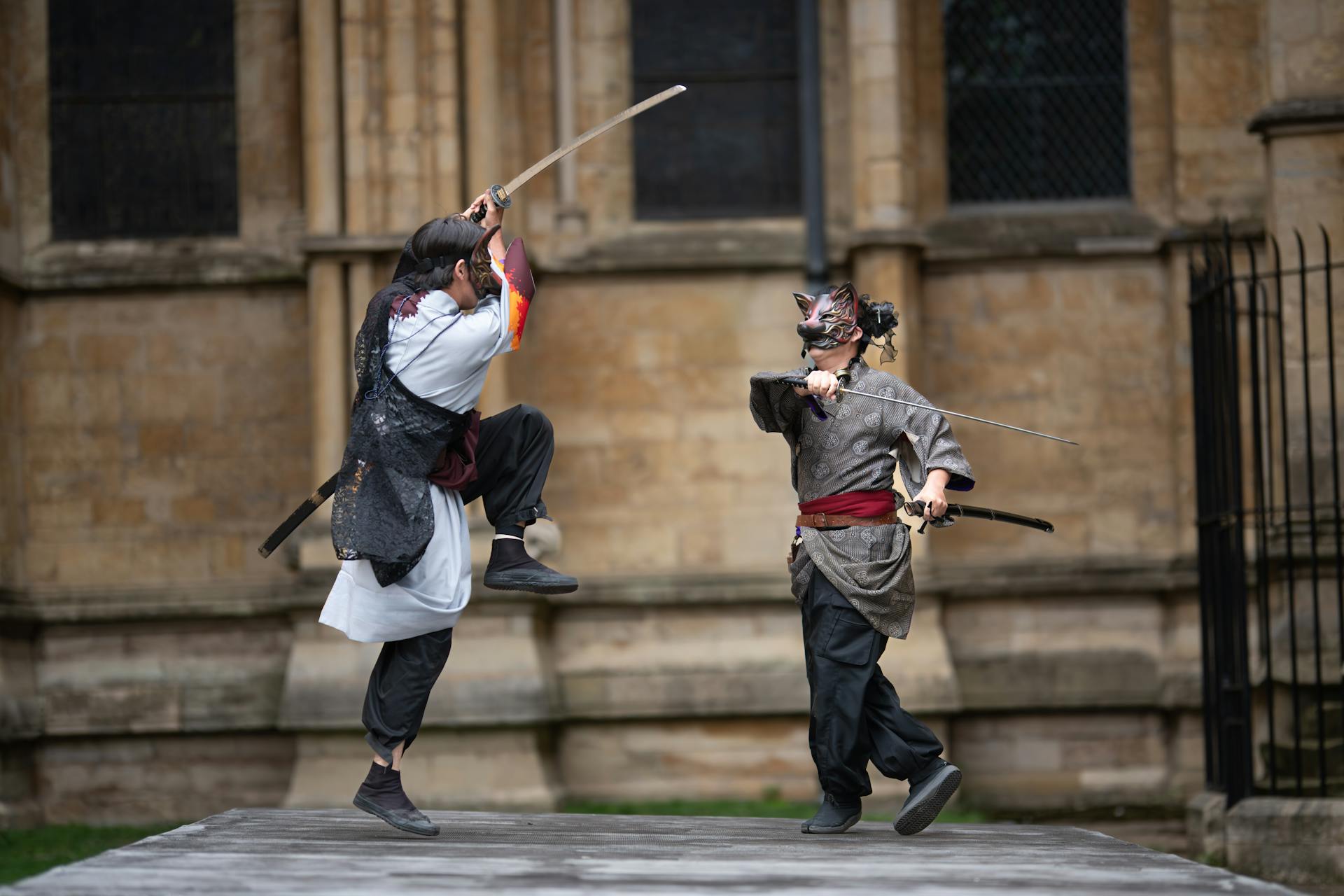 Two people in traditional outfits engaging in a dramatic samurai sword fight outdoors