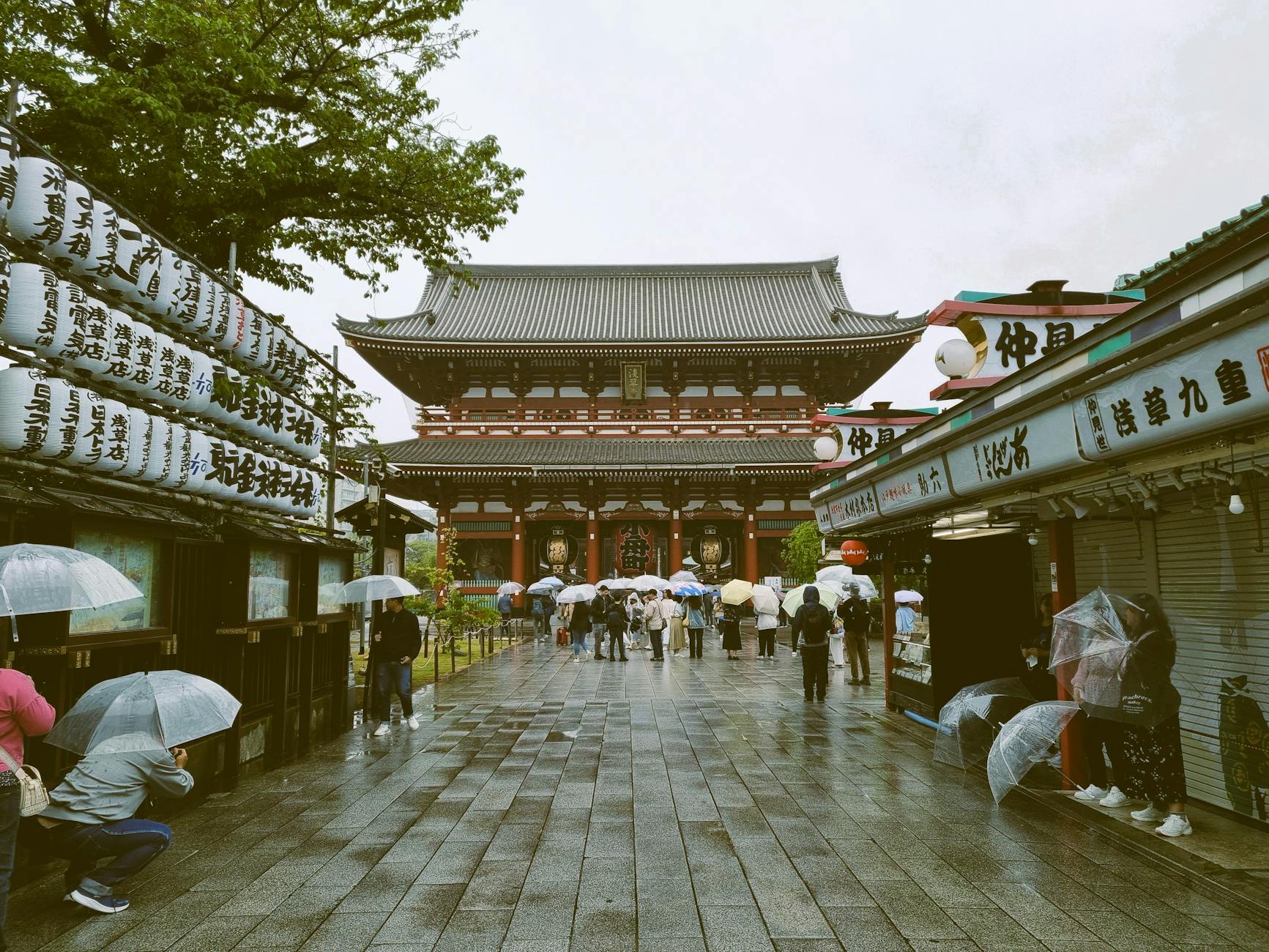 People holding umbrellas in front of the iconic Senso-ji Temple in Tokyo on a rainy day.