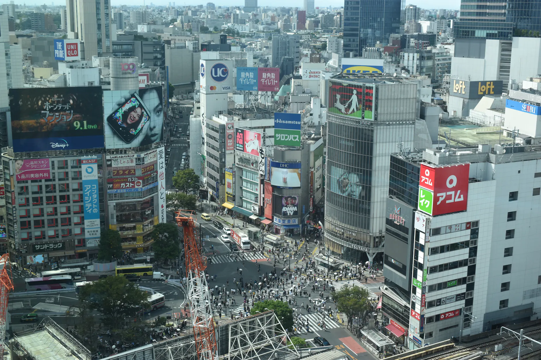 Vibrant aerial view of bustling Shibuya Crossing in Tokyo filled with pedestrians and colorful billboards.