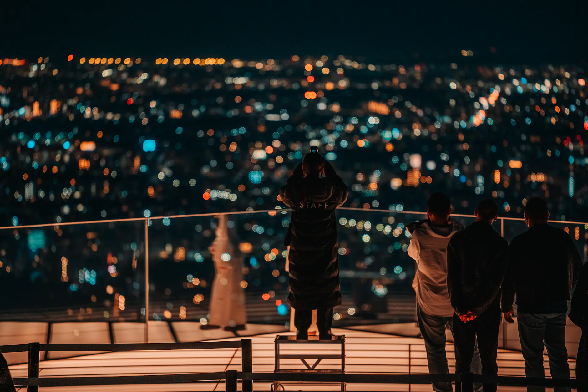 A group overlooking a vibrant nighttime cityscape from a rooftop in Shibuya, Tokyo.