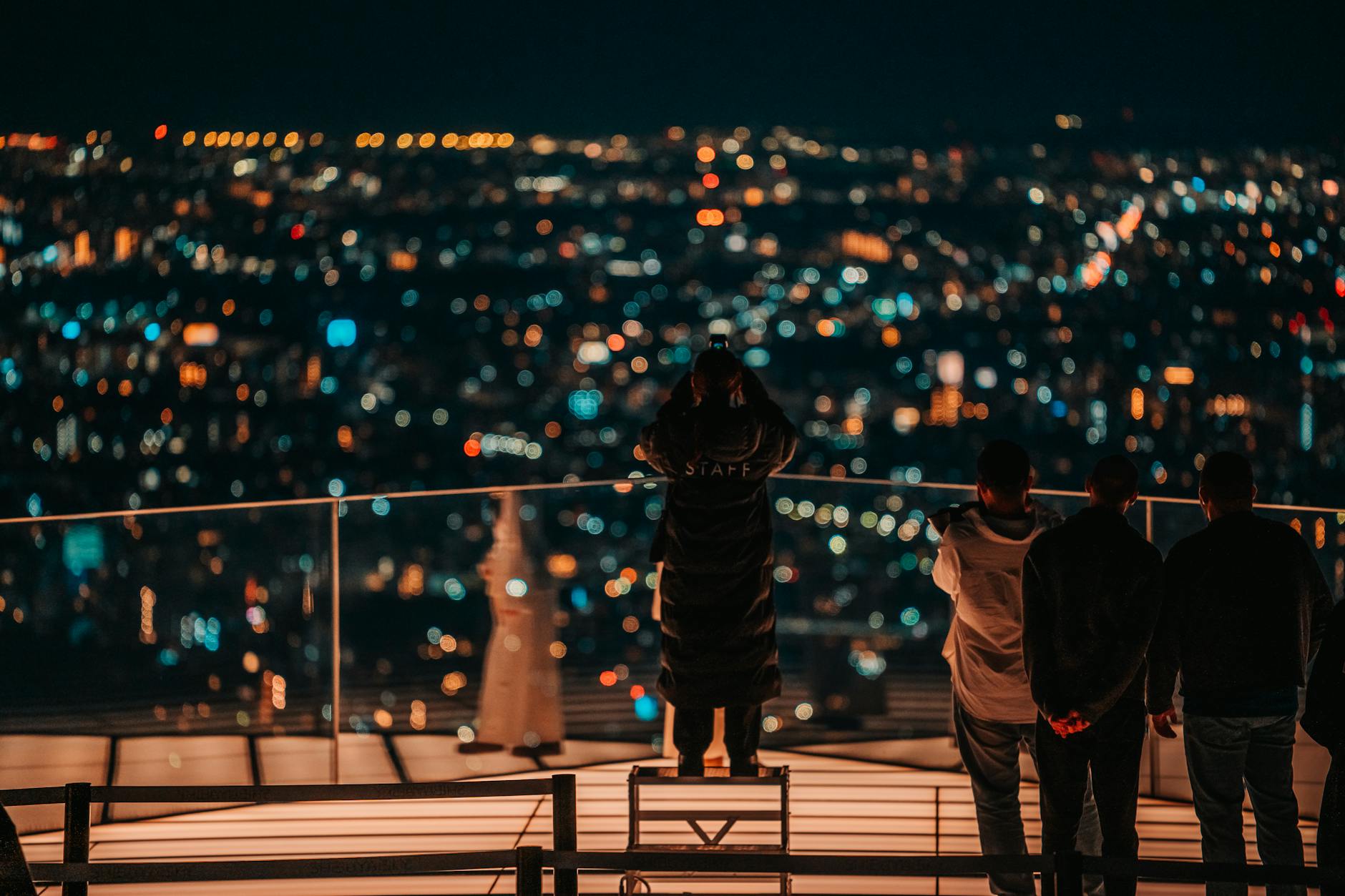 A group overlooking a vibrant nighttime cityscape from a rooftop in Shibuya, Tokyo.