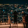 A group overlooking a vibrant nighttime cityscape from a rooftop in Shibuya, Tokyo.