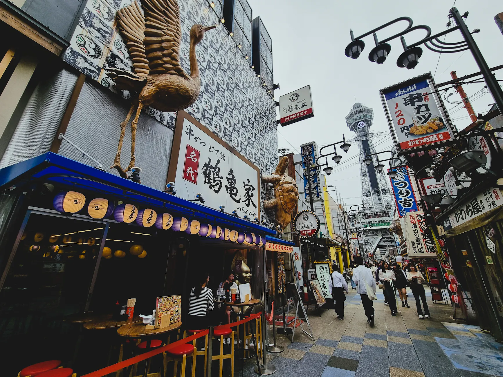 Bustling street in Osaka's Shinsekai district, showcasing local shops and Tsutenkaku Tower.