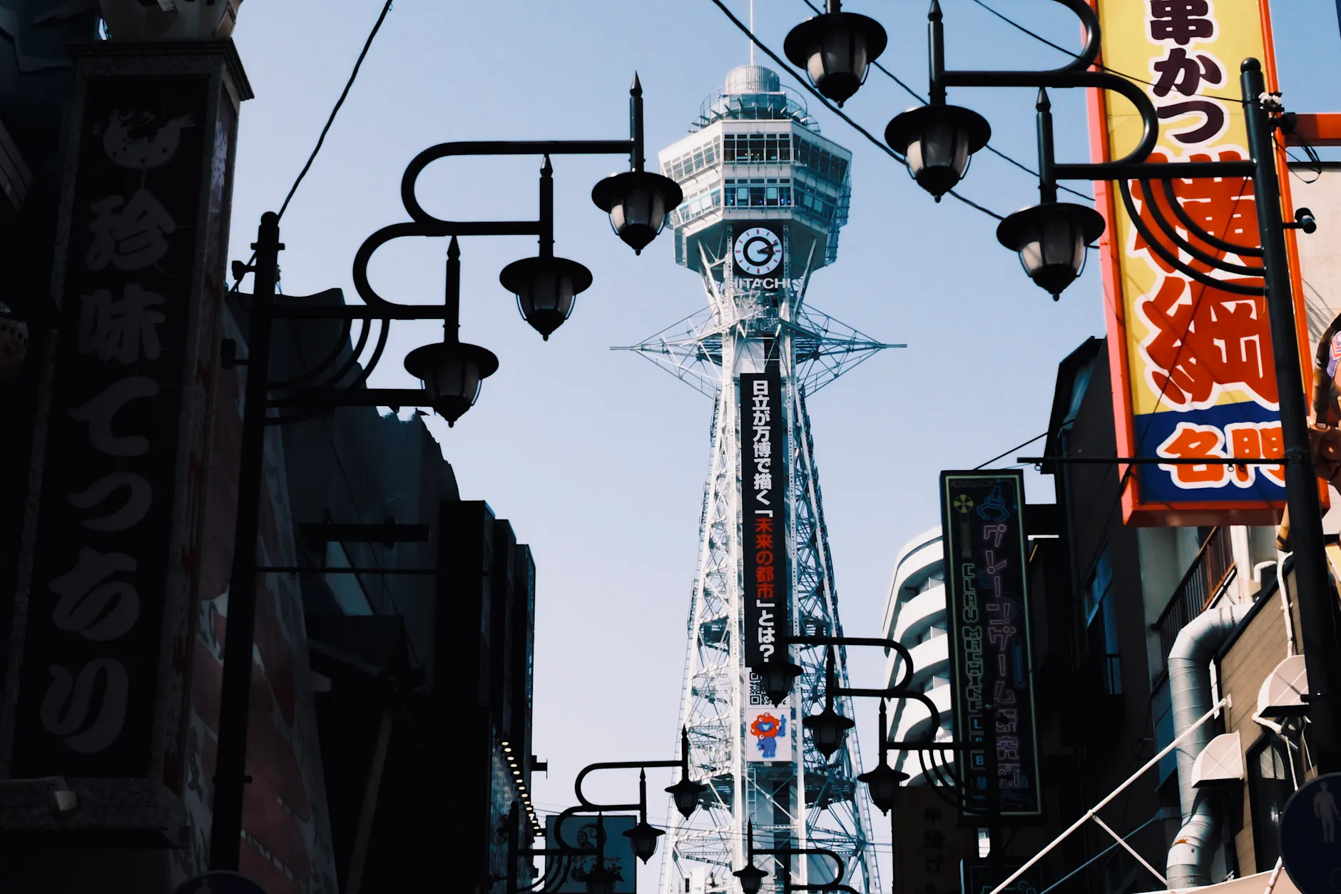 Tsutenkaku Tower in Osaka's vibrant Shinsekai district framed by traditional street lamps.
