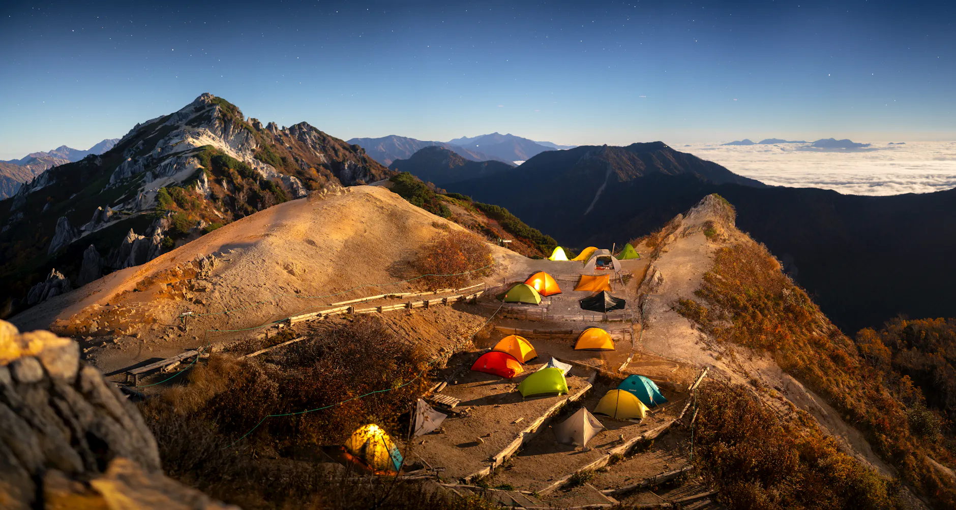 Tents set up on mountain ridge at night in Japanese Alps, under a starlit sky.