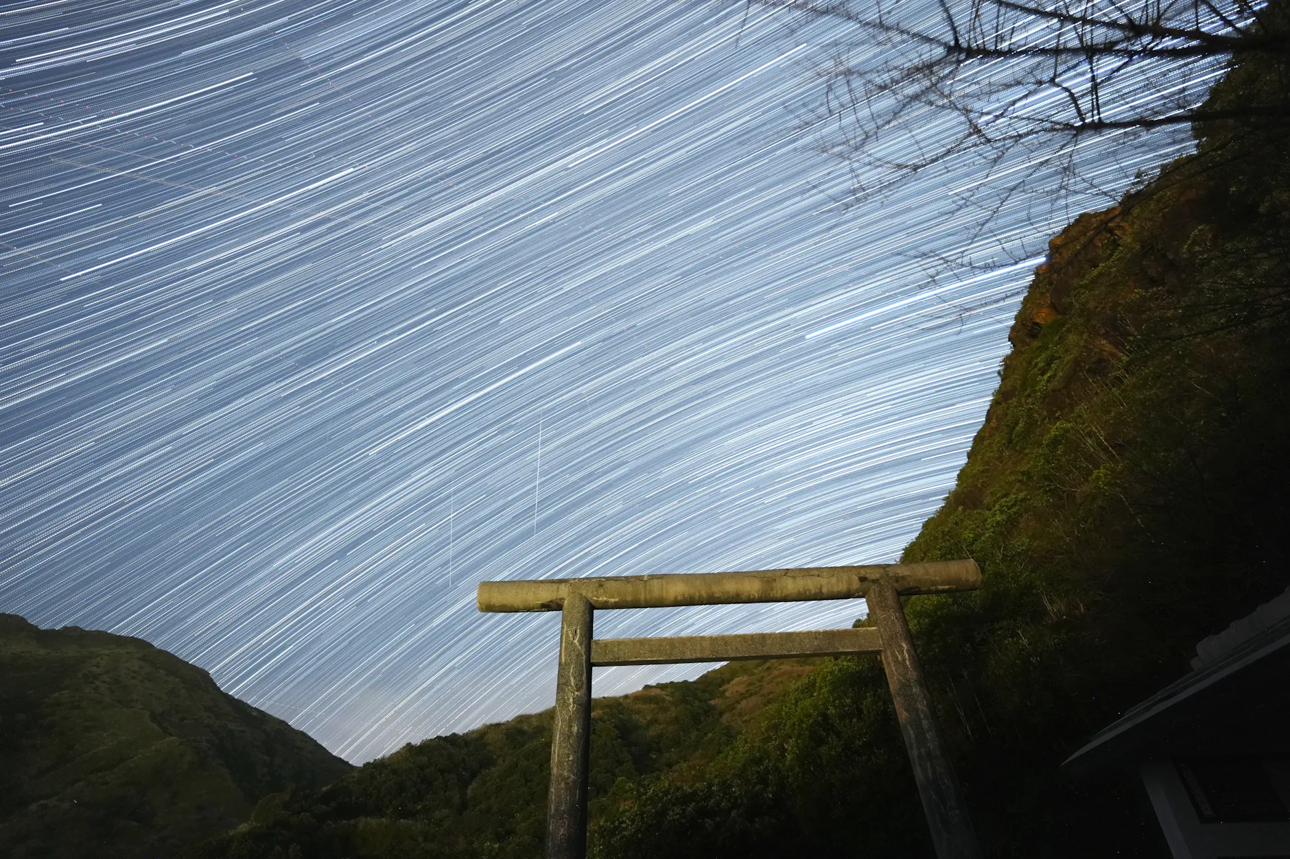 Captivating star trails arc over a traditional Torii gate in a serene night landscape.