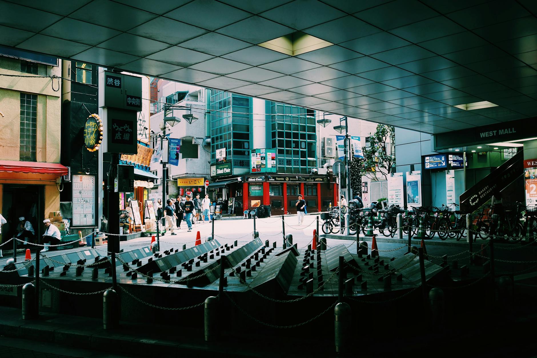 Busy Tokyo street with pedestrians, shops, and bicycles under an urban canopy.